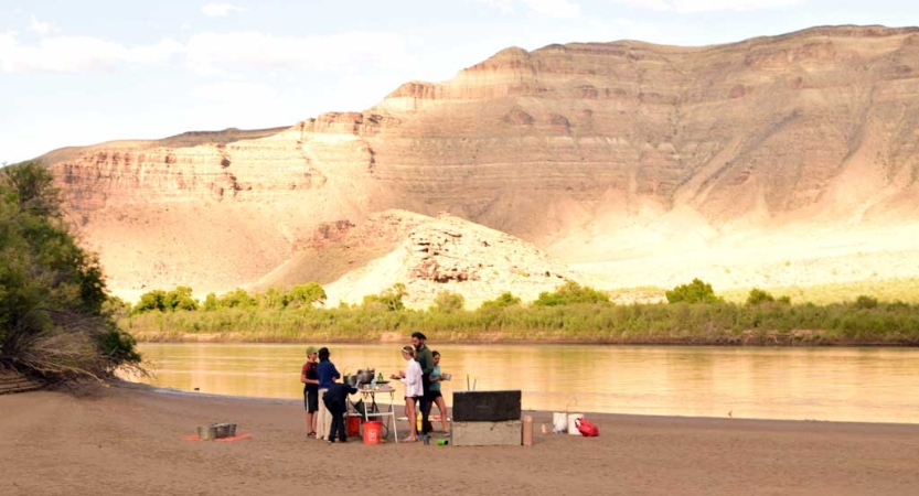 Beside a river with tall canyon walls, a group of people stand on the shore. 
